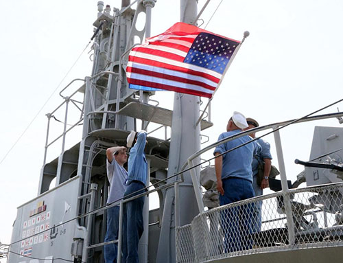 The Dutch and American flags are saluted by sailors of both the Dutch and American Navy.